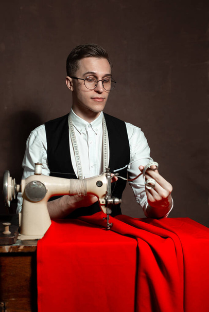 tailor in round glasses sits at a table with a sewing machine - 写真・画像
