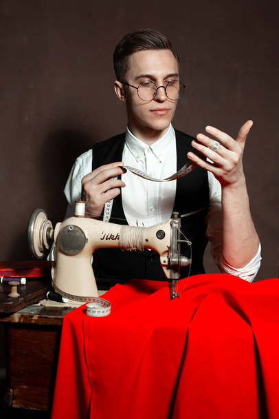alfaiate em copos redondos senta-se em uma mesa com uma máquina de costura
 - Foto, Imagem