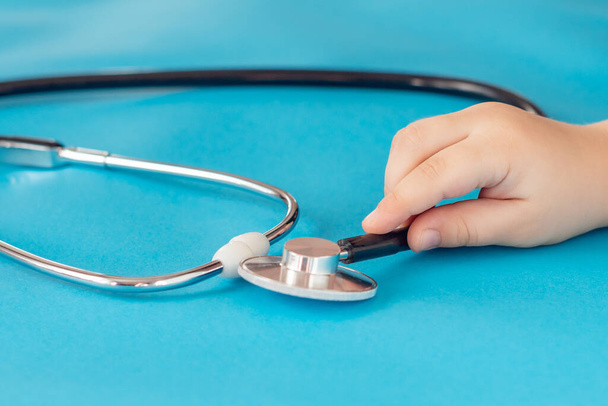 Children's hands hold a medical stethoscope on a blue background. - Photo, Image