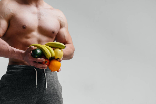 Sporty, naked torso of an athlete with fruit on a white background. Fitness. Healthy diet - Foto, Bild