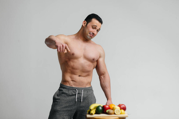 Szexi vega srác meztelen felsőtesttel, aki a stúdióban pózol a gyümölcs mellett. Fogyókúra. Egészséges táplálkozás - Fotó, kép
