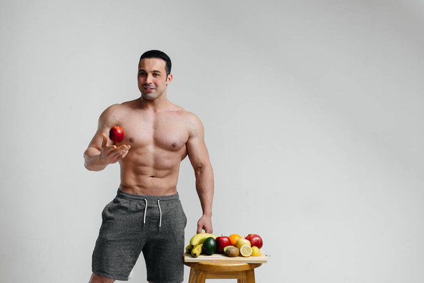 Sporty mec sexy posant sur un fond blanc avec des fruits brillants. Régime alimentaire. Une alimentation saine - Photo, image