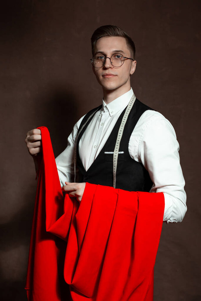 портниха в круглых очках и классической одежде с красной тканью
 - Фото, изображение
