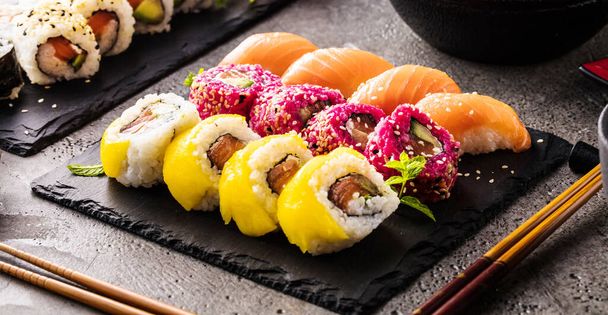 close-up view of delicious sushi set on slate boards and chopsticks on black surface - Фото, изображение