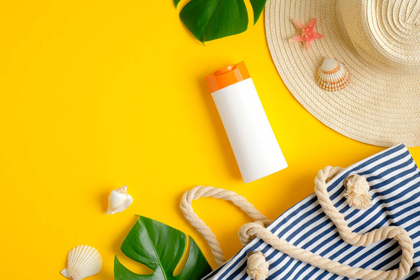 Top view suntan cream bottle, beach bag, female hat and tropical leaves on yellow background. Sun protection on summer vacation concept - Foto, Imagem