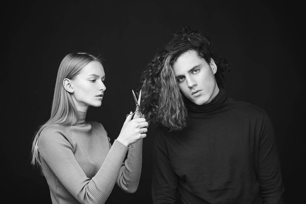 Hair salon concept. Hairdresser girl going to cut off long wavy bleached dry hair of customer man. Man hair style, wellness and fashion. Female with scissors going to do amazing man haircut. - 写真・画像