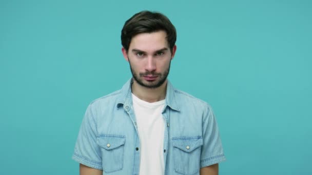 Dismal upset young bearded guy in jeans shirt looking at camera with serious depressed gloomy face, experiencing midlife crisis, negative emotions. indoor studio shot isolated on blue background - Materiał filmowy, wideo