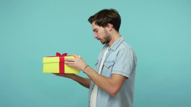 Nice guy unwrapping gift and expressing extreme joy, satisfied with perfect birthday surprise, embracing box saying I'm happy, celebrating holidays. indoor studio shot isolated on blue background - Кадри, відео