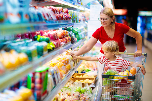 Ψώνια με παιδιά. Μητέρα και παιδί αγοράζουν φρούτα στο σούπερ μάρκετ. Η μαμά και το αγοράκι αγοράζουν φρέσκο μάνγκο στο μανάβικο. Οικογένεια στο κατάστημα. Γονείς και παιδιά σε ένα εμπορικό κέντρο που επιλέγουν λαχανικά. Υγιή τρόφιμα. - Φωτογραφία, εικόνα