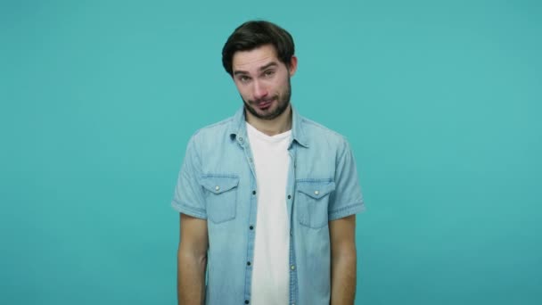 Positive male employee asking for salary increase, bearded guy in jeans shirt smiling to camera and showing money gesture, needs more cash, financial reward. studio shot isolated on blue background - Metraje, vídeo