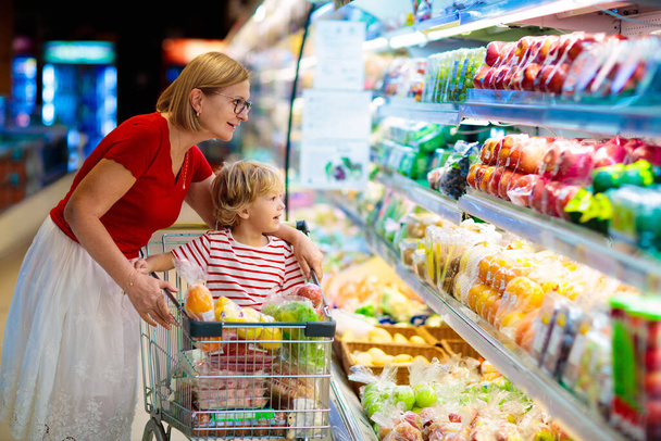 Shopping with kids. Mother and child buying fruit in supermarket. Mom and little boy buy fresh mango in grocery store. Family in shop. Parent and children in a mall choosing vegetables. Healthy food. - 写真・画像