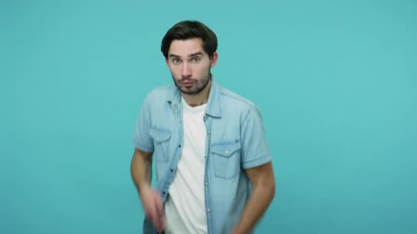 Bearded guy in jeans shirt pretending to be cowboy, grasping finger pistol and pointing to camera, shooting right on target, gesturing weapon, killing. indoor studio shot isolated on blue background - Imágenes, Vídeo