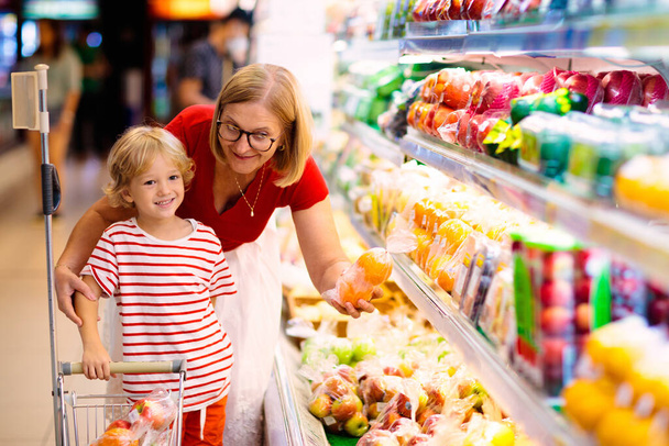 Einkaufen mit Kindern. Mutter und Kind kaufen Obst im Supermarkt. Mutter und kleiner Junge kaufen frische Mango im Lebensmittelgeschäft. Familie im Geschäft. Eltern und Kinder in einem Einkaufszentrum bei der Auswahl von Gemüse. gesunde Ernährung. - Foto, Bild