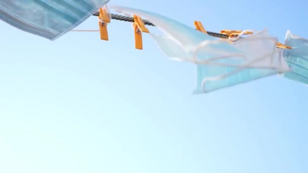 Máscaras médicas azules colgando en un tendedero con pinzas de ropa contra el cielo
 - Imágenes, Vídeo