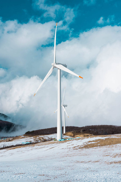 Elektrische Turbine Windmolen op een blauwe lucht en besneeuwde grond. Close-up beeld van turbines messen op een heuvel vol sneeuw. - Foto, afbeelding