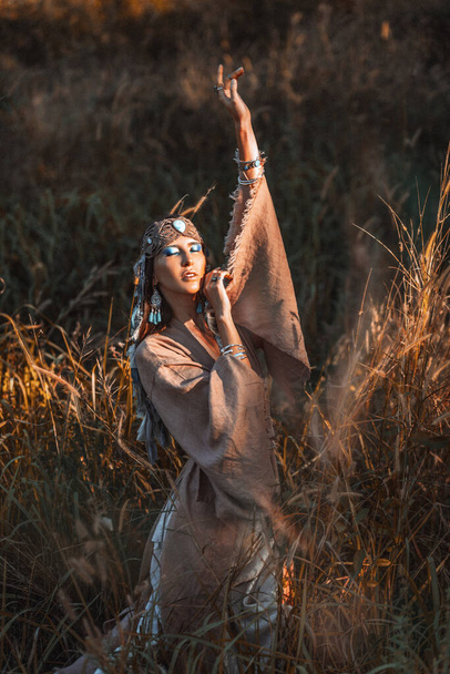 Beautiful young stylish woman on the field at sunset. Oriental tribal princess - 写真・画像