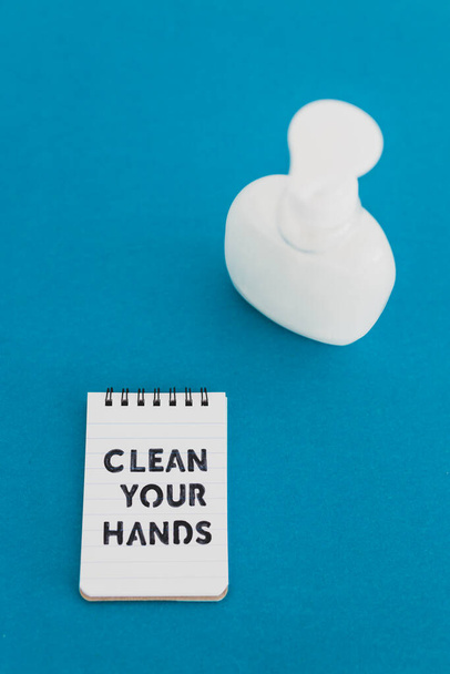 keep your hands clean to fight bacteria and viruses conceptual still-life, liquid soap next to memo with Clean your Hands text on blue background - 写真・画像