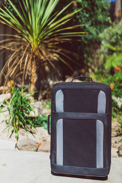 concept of summer holidays, suitcase with tropical garden bokeh behind it concept of travelling to warm tropical destinations - Foto, Imagem
