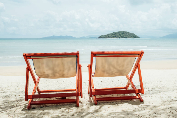 Два лежака на красивом песчаном пляже с чистой водой и остров на заднем плане - Фото, изображение