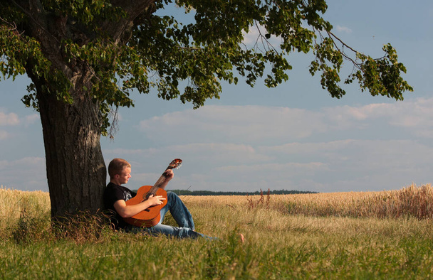 young man playing guitar in the field - Foto, Imagem