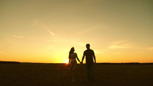 beautiful girl and guy go hand in hand in rays of sun in spring. happy family walking in park in summer, happy family concept. A young couple in love walks and listens to music on a smartphone. - Foto, Bild