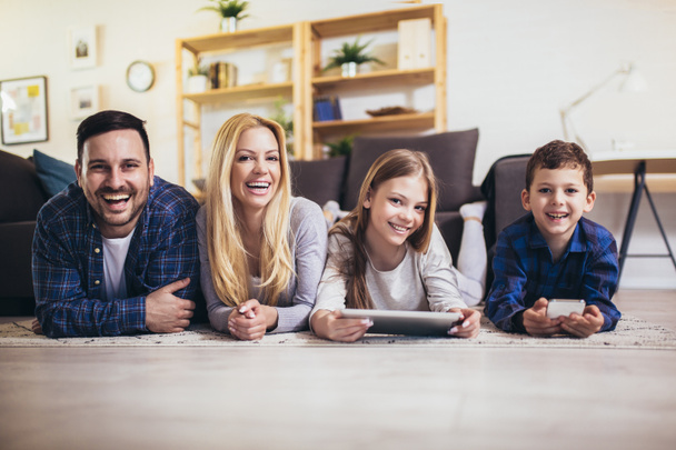 Junge vierköpfige Familie entspannt sich am Wochenende auf dem Fußboden im Wohnzimmer und schaut Filme oder Zeichentrickfilme auf dem digitalen Tablet - Foto, Bild