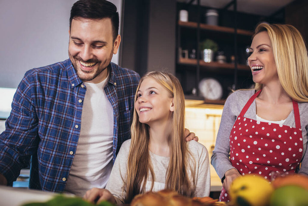 Kız ve güzel ailesi evde yemek pişirirken sebze kesip gülümsüyorlar. - Fotoğraf, Görsel