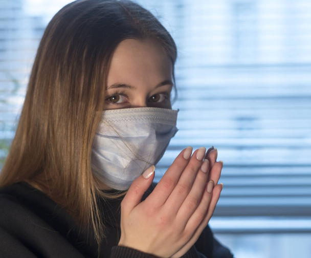 Πρόληψη της εξάπλωσης της νόσου του Coronavirus 2019 (Covid-19). Νεαρή γυναίκα που κοιτάζει την κάμερα φτερνίζεται ή βήχει με προστατευτική μάσκα προσώπου - Φωτογραφία, εικόνα