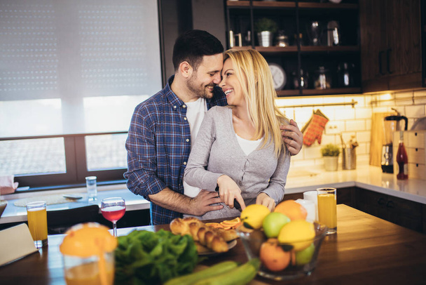美しい若いカップルは、自宅でキッチンで健康的な食べ物を調理しながら話して笑顔です. - 写真・画像