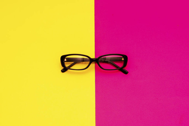 Black modern eye glasses on red and yellow background. - Photo, Image