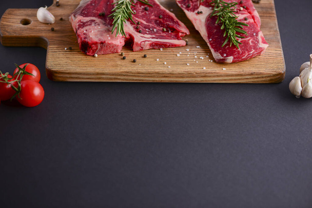 Fresh raw steak on wooden cutting board over black background with spices, top view. - Fotoğraf, Görsel