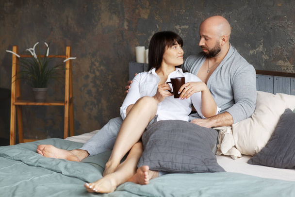 Carino giovane coppia bere caffè mattutino sdraiato a letto. Amore e relazioni, marito e moglie, fidanzato e fidanzata
 - Foto, immagini