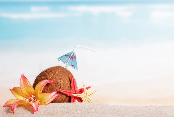 Coconut, starfish and flower in the sand against the sea. - Φωτογραφία, εικόνα