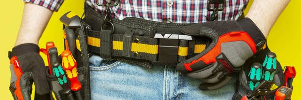 Electrician or professional Builder in the installer's belt with tools on a yellow background. Electrician's tools in black bags on the worker 's belt. Banner with space for text - Foto, immagini