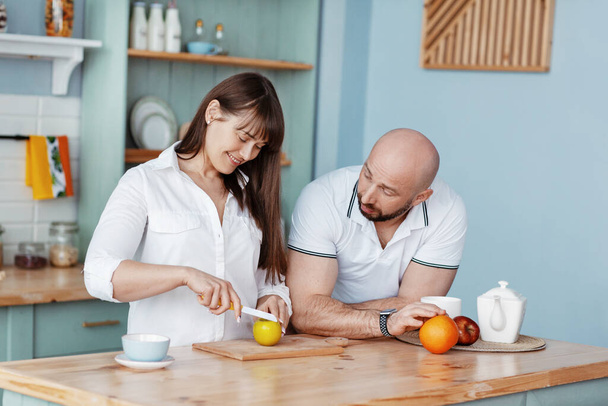 Ένα νεαρό όμορφο ζευγάρι ετοιμάζει πρωινό μαζί στην κουζίνα το πρωί του Σαββατοκύριακου. Ρομαντικές σχέσεις, αγάπη, οικογένεια - Φωτογραφία, εικόνα