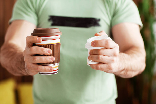 Muž drží opakovaně použitelný pohár v jedné ruce a plastový pohár v druhé. Proti použití jednorázového plastu. Správná volba, volba životního prostředí - Fotografie, Obrázek