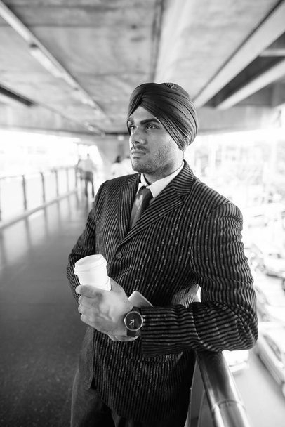 Portré fiatal jóképű indiai szikh üzletemberről, aki turbánt visel, miközben felfedezi a várost fekete-fehérben. - Fotó, kép