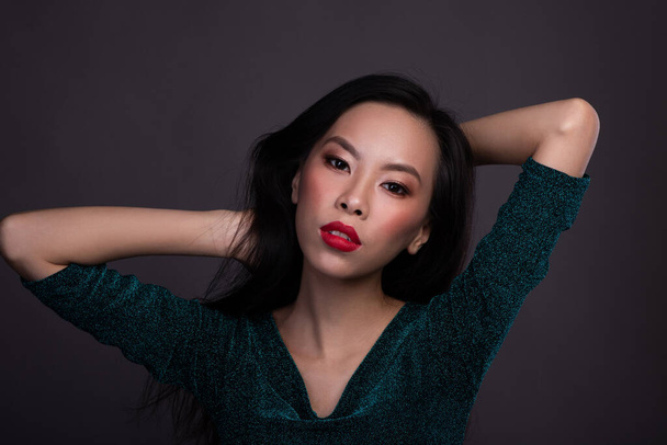 Porträt einer Asiatin mit roten Lippen im Kleid im Studio vor dunklem Hintergrund - Foto, Bild