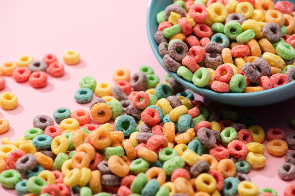 bright colorful breakfast cereal scattered from bowl on pink background - Fotó, kép