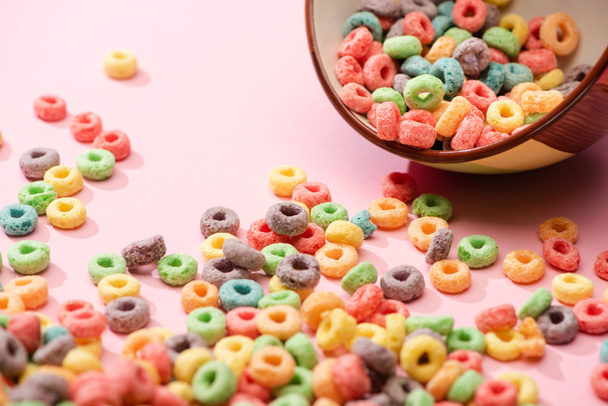 selective focus of bright colorful breakfast cereal scattered from bowl on pink background - Foto, afbeelding