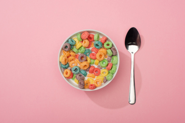 top view of bright colorful breakfast cereal in bowl near spoon on pink background - Foto, Imagem