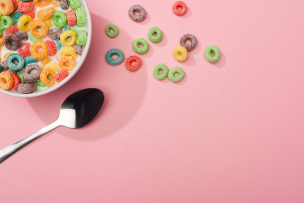 top view of bright colorful breakfast cereal with milk in bowl near spoon on pink background - Фото, зображення