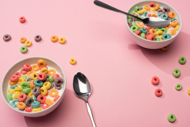 selective focus of bright colorful breakfast cereal with milk in bowls with spoons on pink background - Photo, Image