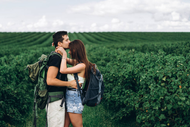 Portrait of happy young couple with backpacks on the field in spring. Man and woman walking in currant plantations. - Fotografie, Obrázek