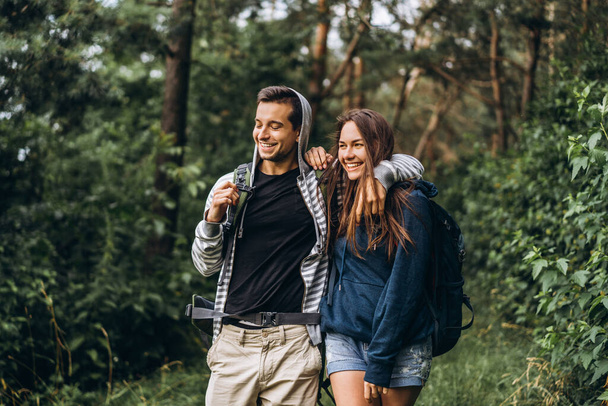 Young couple with backpacks on their backs smiling and walking in the forest, enjoy the walk. - Фото, изображение