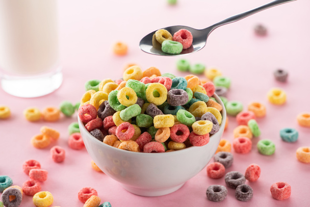 selective focus of bright multicolored breakfast cereal in bowl near glass of milk and spoon on pink background - Foto, Imagem