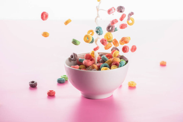 bright multicolored breakfast cereal in bowl with milk splash on pink background - Фото, изображение