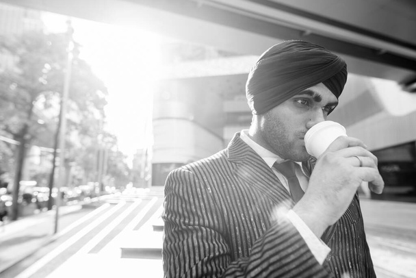 Portré fiatal jóképű indiai szikh üzletemberről, aki turbánt visel, miközben felfedezi a várost fekete-fehérben. - Fotó, kép