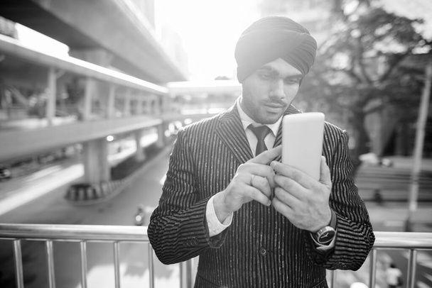黒と白の街を探索しながらターバンを身に着けている若いハンサムなインドのシークのビジネスマンの肖像画 - 写真・画像