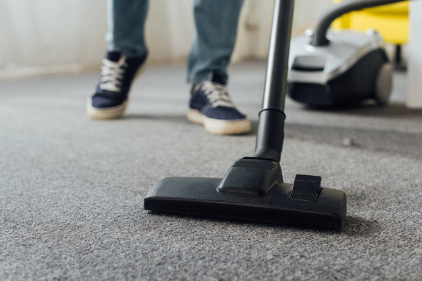 Cropped view of man cleaning carpet with vacuum cleaner at home  - Foto, imagen